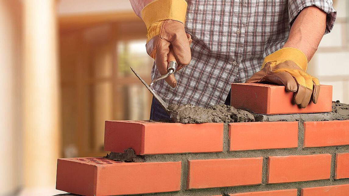 ein Arbeiter baut eine Mauer mit Ziegelsteinen