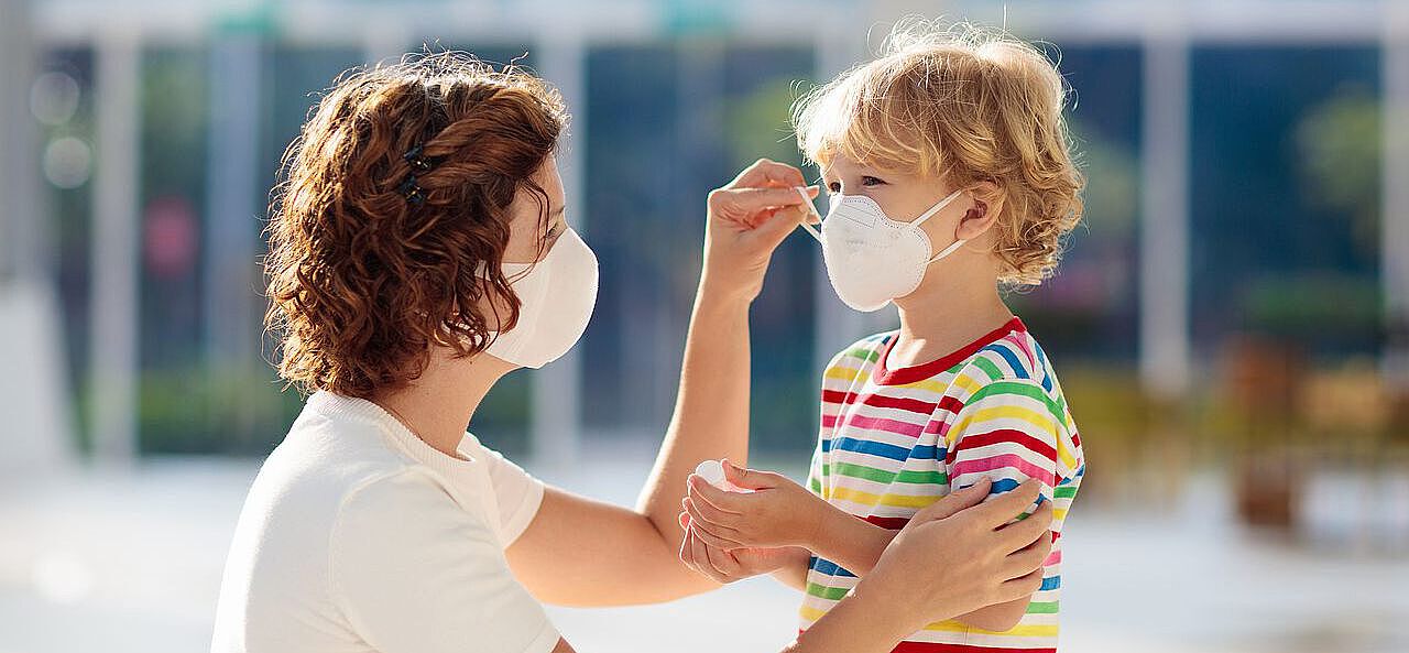 Mutter hilft Kind beim Anziehen einer Alltagsmaske