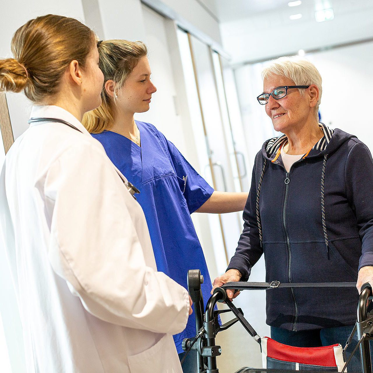 Medizinisches Fachpersonal betreut eine ältere Patientin mit Rollator.