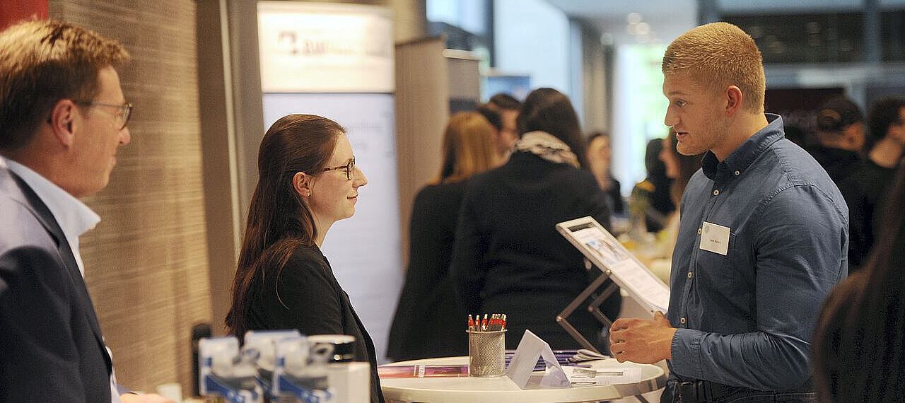 Ein Student unterhält sich mit auf der Job- und Praktikumsbörse mit zwei Unternehmensvertretern an deren Stand