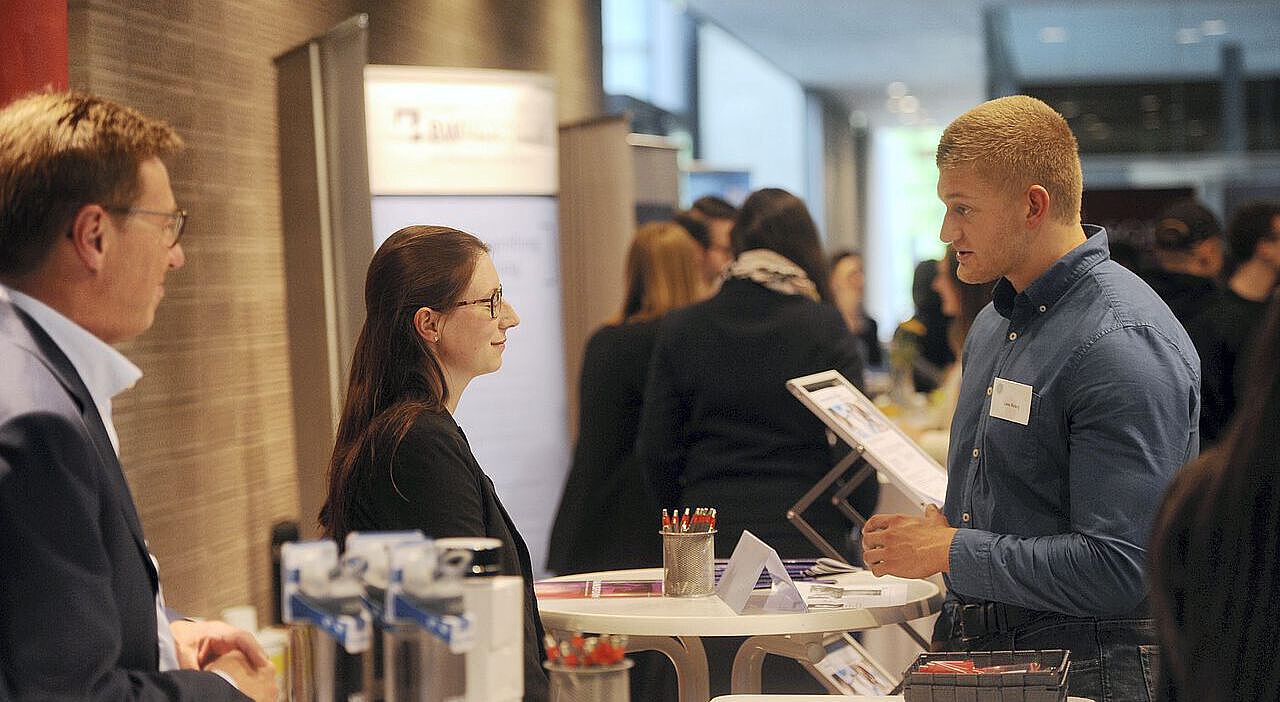 Ein Student unterhält sich mit auf der Job- und Praktikumsbörse mit zwei Unternehmensvertretern an deren Stand
