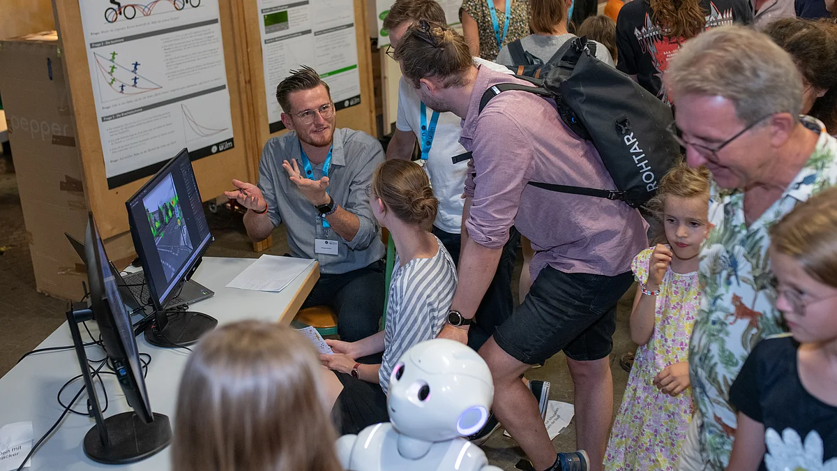 Besucher*innen am Stand des Instituts für Business Analytics mit mit Roboter Pepper und Eyetracker Tobii 