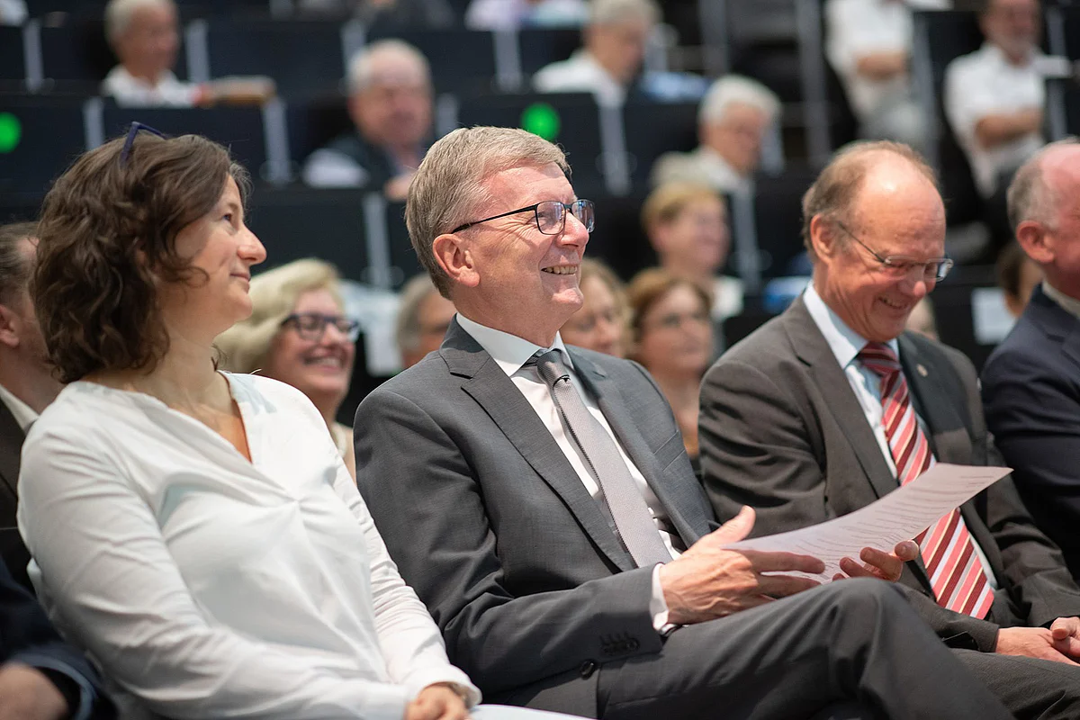Dieter Kaufmann is sitting in the front row of the lecture theatre, laughing, with a sheet of paper in his hand