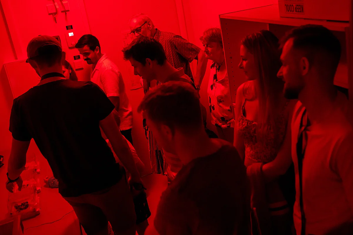 Eine Gruppe Menschen in einem dunklen, rötlich leuchtenden Raum. 