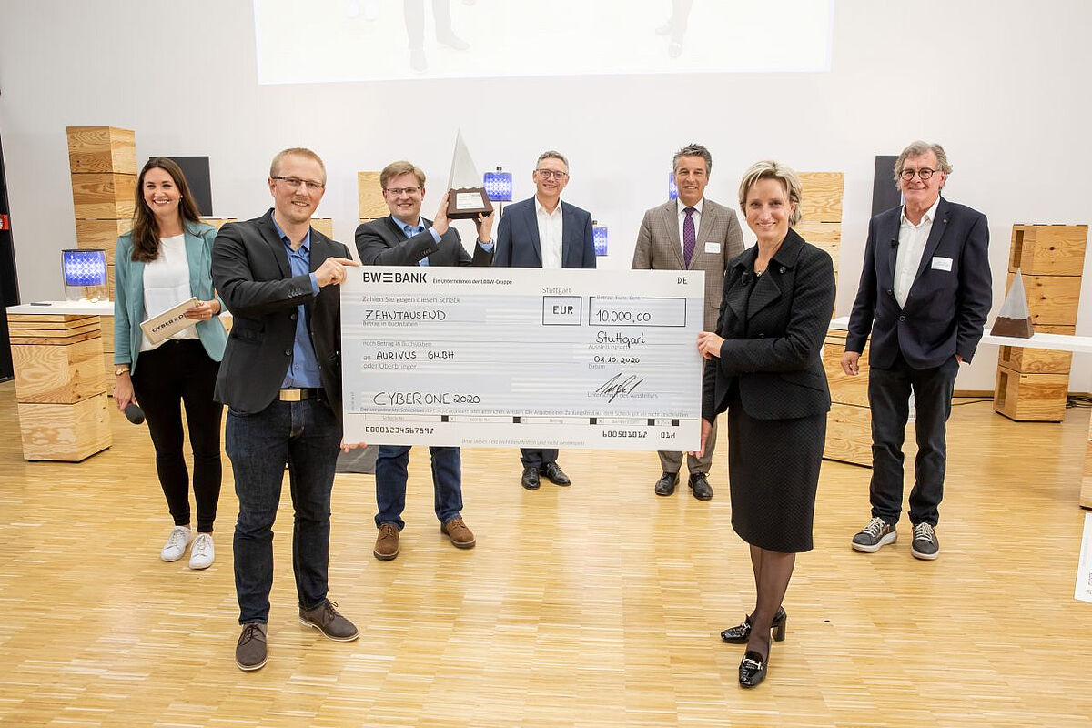 Die Wirtschaftsministerin von Baden-Württemberg, Dr. Nicole Hoffmeister-Kraut (vorne rechts), übergibt den CyberOne-Preis-Scheck an die Aurivus-Unternehmensgründer Martin Bach (vorne links) und Dr. Stefan Hörmann mit Pyramide