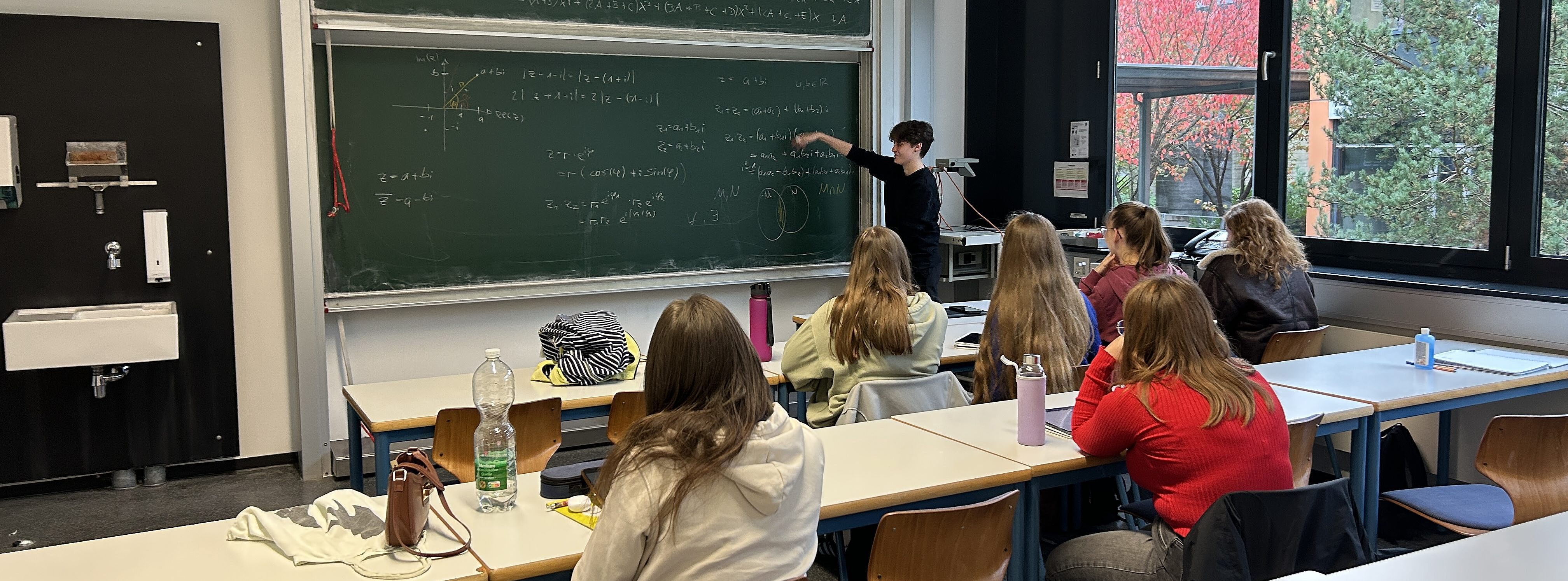 Tutorin steht vor Klasse mit Erstsemestern an der Tafel