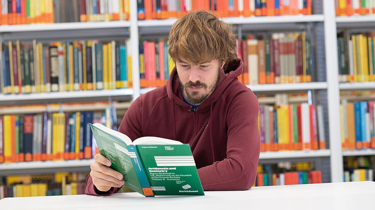 Student sitzt vor einem Buch in der Bib