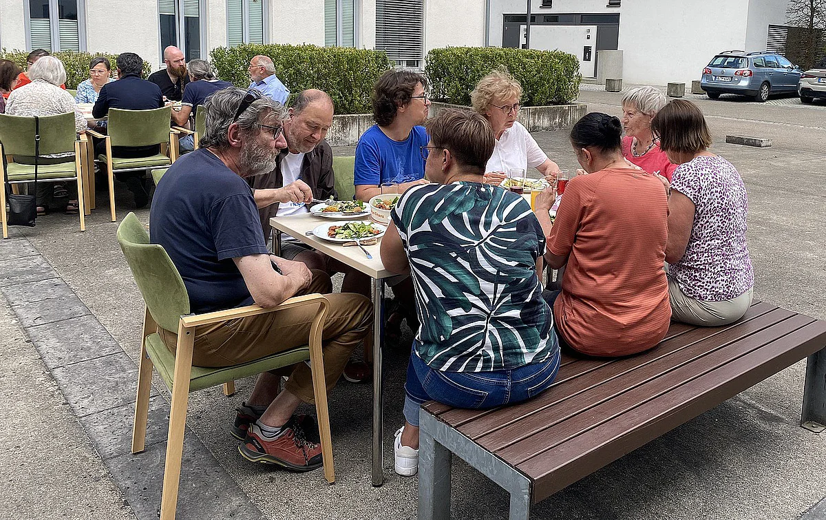 An Tischen sitzen Teilnehmende unter freiem Himmel, essen und reden gemeinsam.
