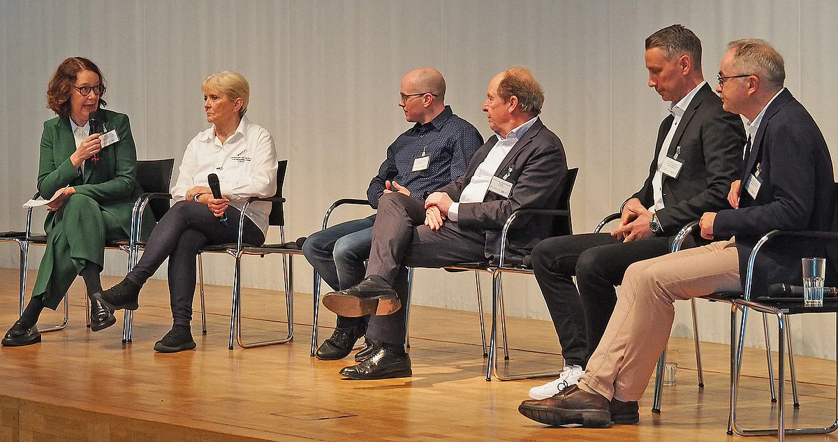 Diskussionsteilnehmende sitzen auf einer Bühne nebeneinander