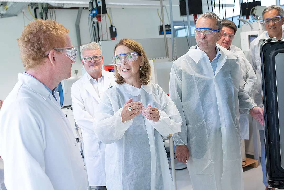 Petra Olschowski, Prof. Maximilian Fichtner und Prof. Michael Kühl in weißen Laborkitteln und Laborbrillen