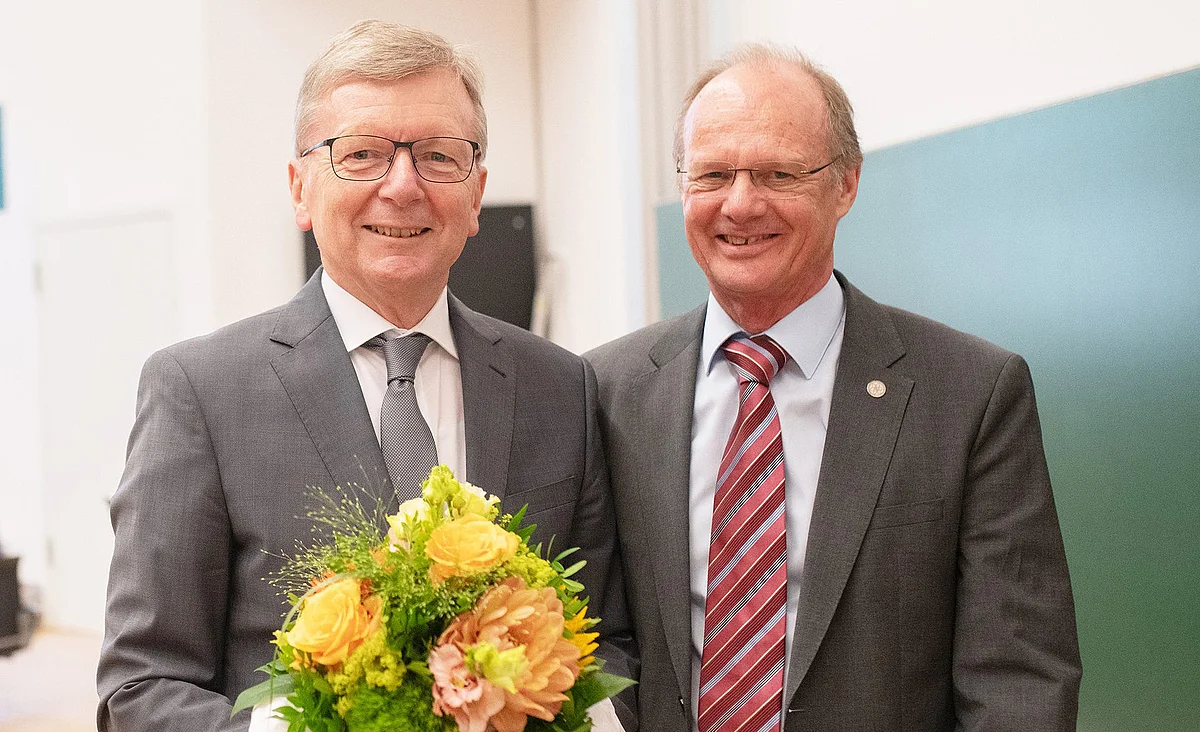 Deiter Kaufmann (left) stands next to Prof. Michael Weber, holding a bouquet of flowers; both are smiling