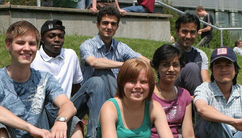 Eine Gruppe internationaler Studierender im Sommer sitzend im Gras. 