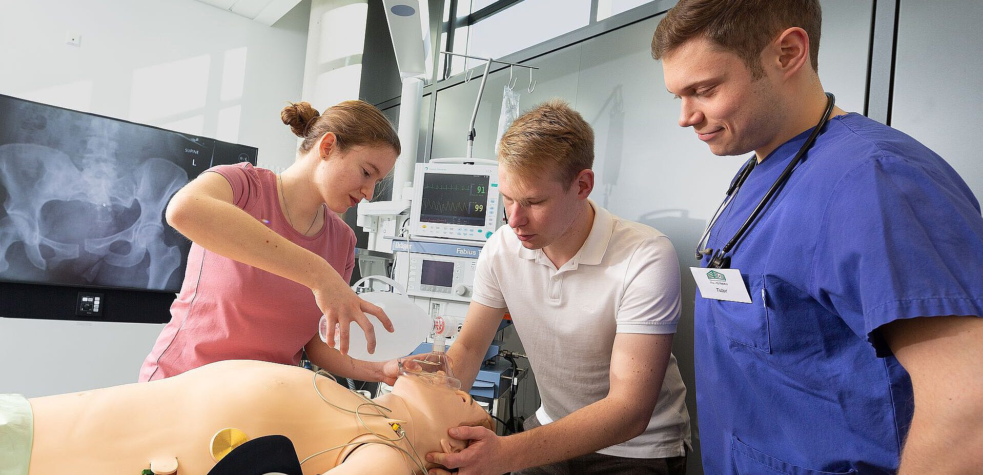 Drei junge Menschen bereiten eine Simulationspuppe auf die Narkose vor