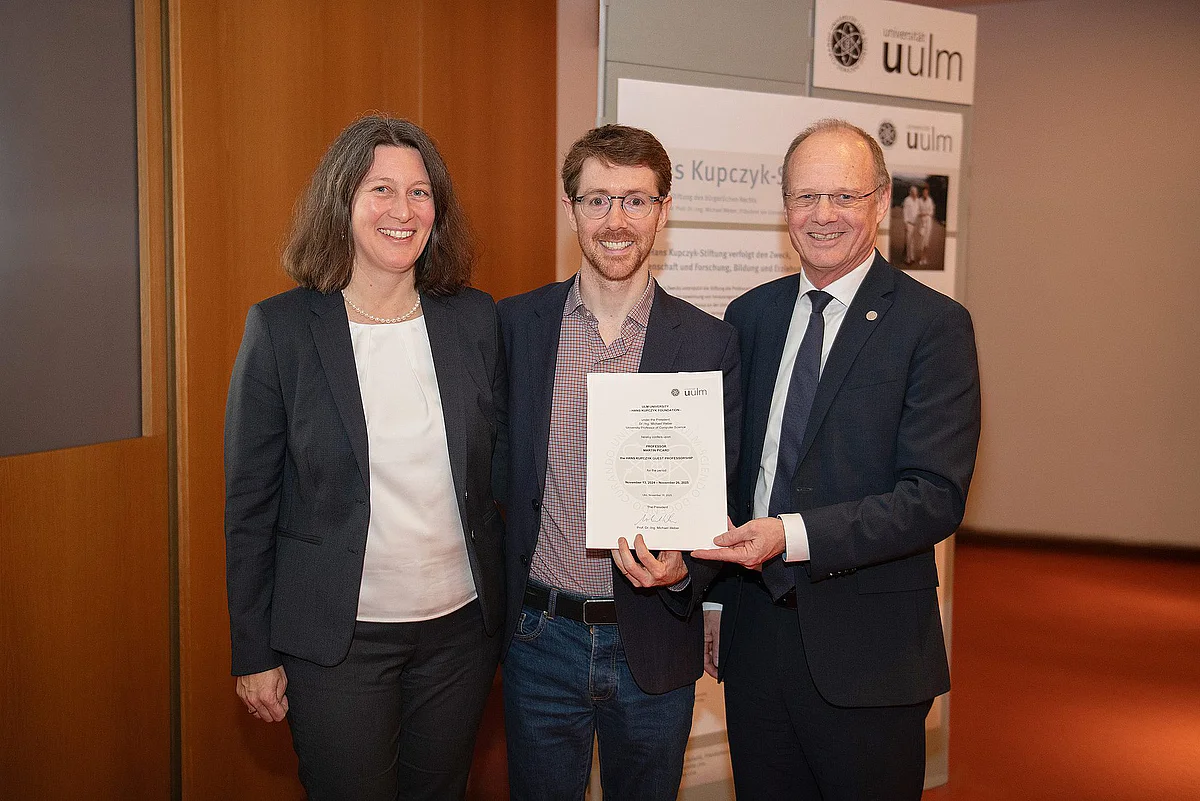 Prof. Martin Picard (centre) with Prof. Iris-Tatjana Kolassa and University President Prof. Michael Weber with the certificate of appointment