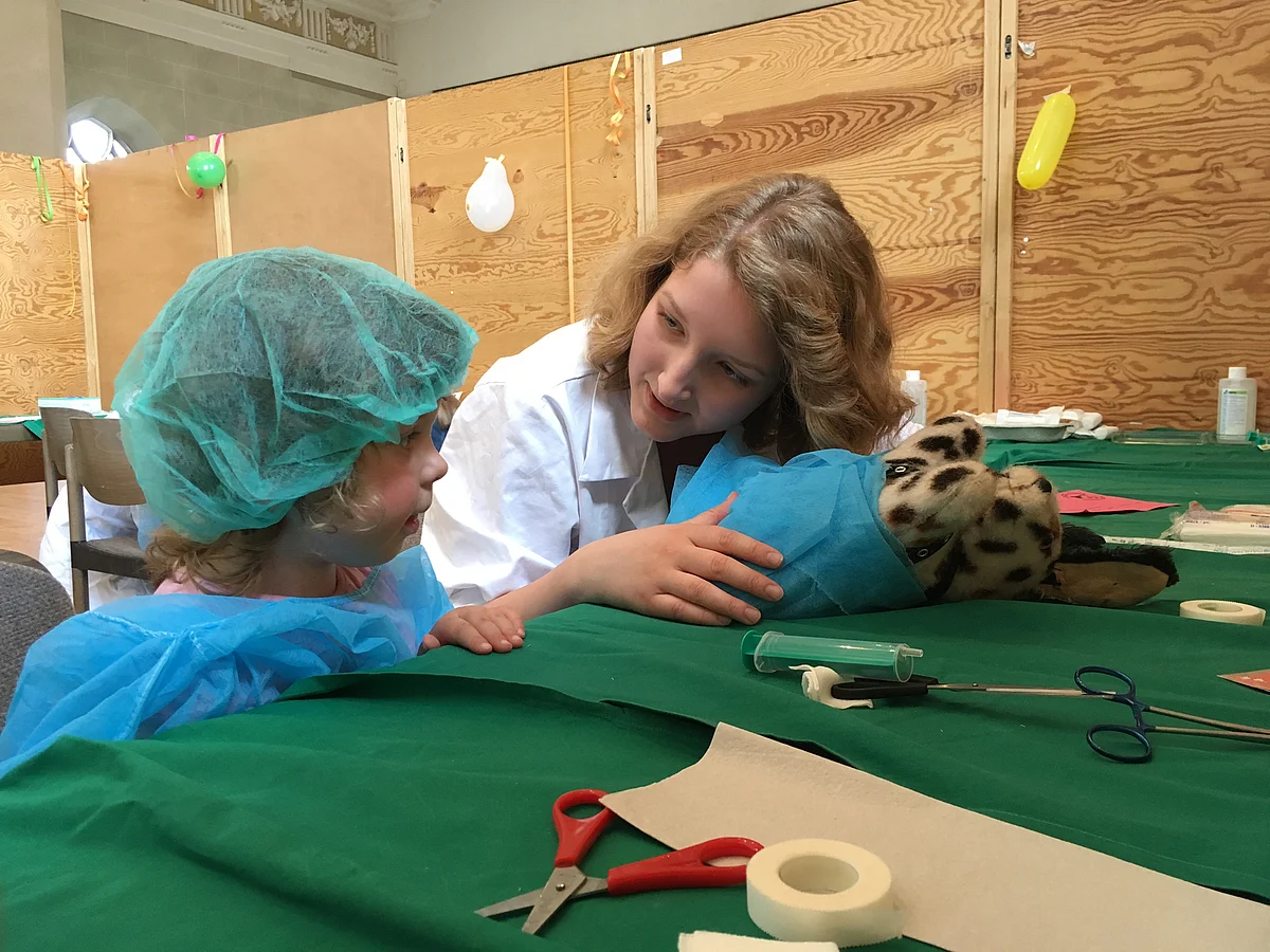 Kind und Studentin behandeln einen Teddy in der Teddyklinik