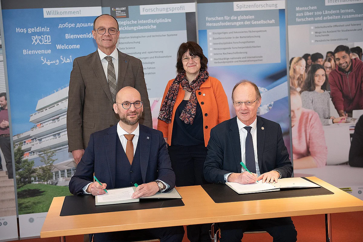 Group photo in front of roll-ups from Ulm University: Prof Kim-Patrick Sabla-Dimitrov (left) and Prof Michael Weber sit at a table and sign the cooperation agreement for the Gmünd Ulm School of Education. Behind them are Edgar Buhl and Prof Olga Pollatos