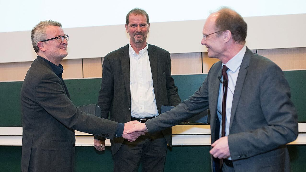 Collaboration at Ulm University President Weber shaking hands and congratulating two leading scientists of Ulm University