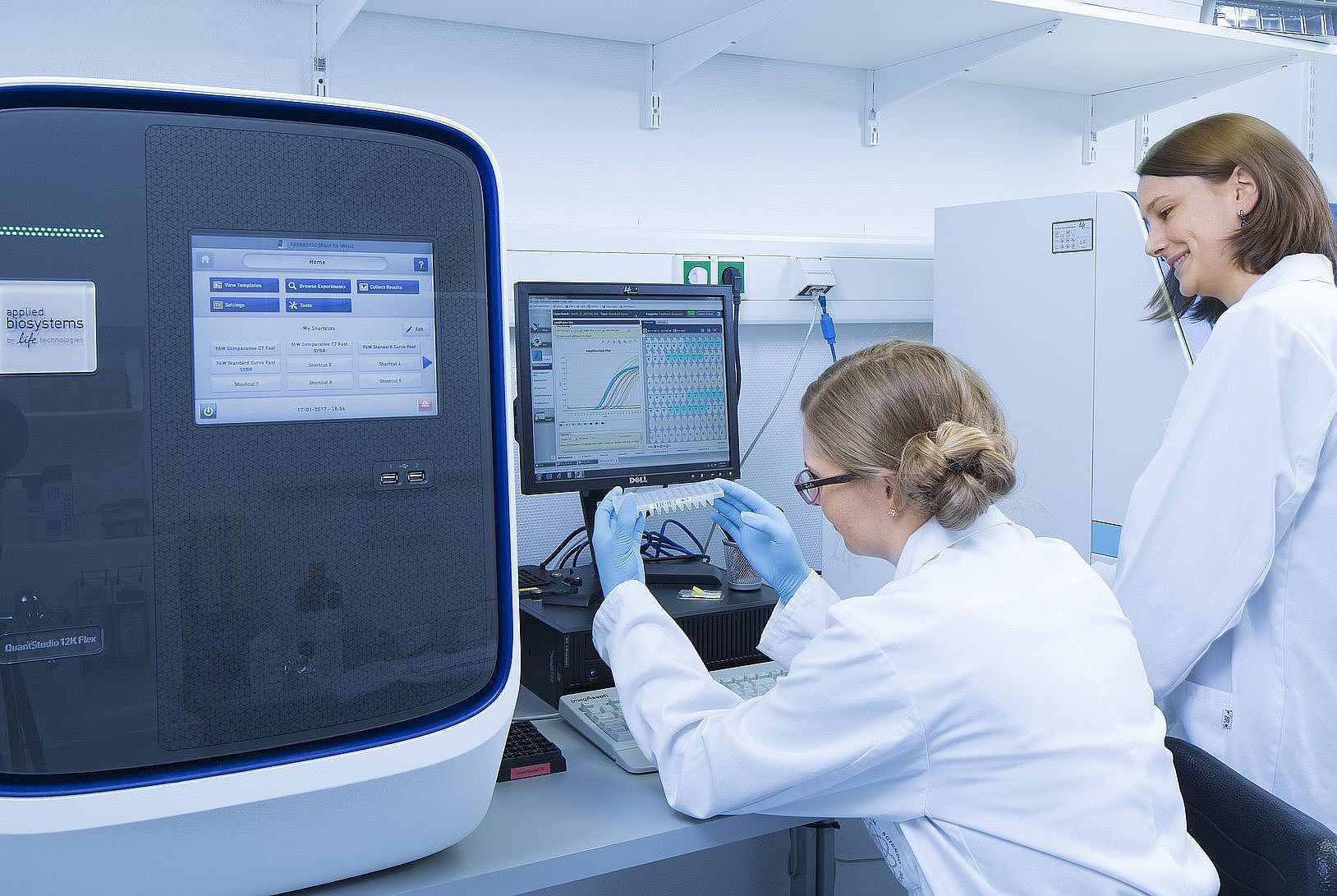 Zwei Forscherinnen in weißen Laborkitteln arbeiten an Laborgeräten in einem Genlabor.