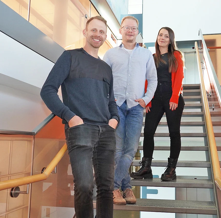Two men and a woman stand next to each other on a staircase, all smiling