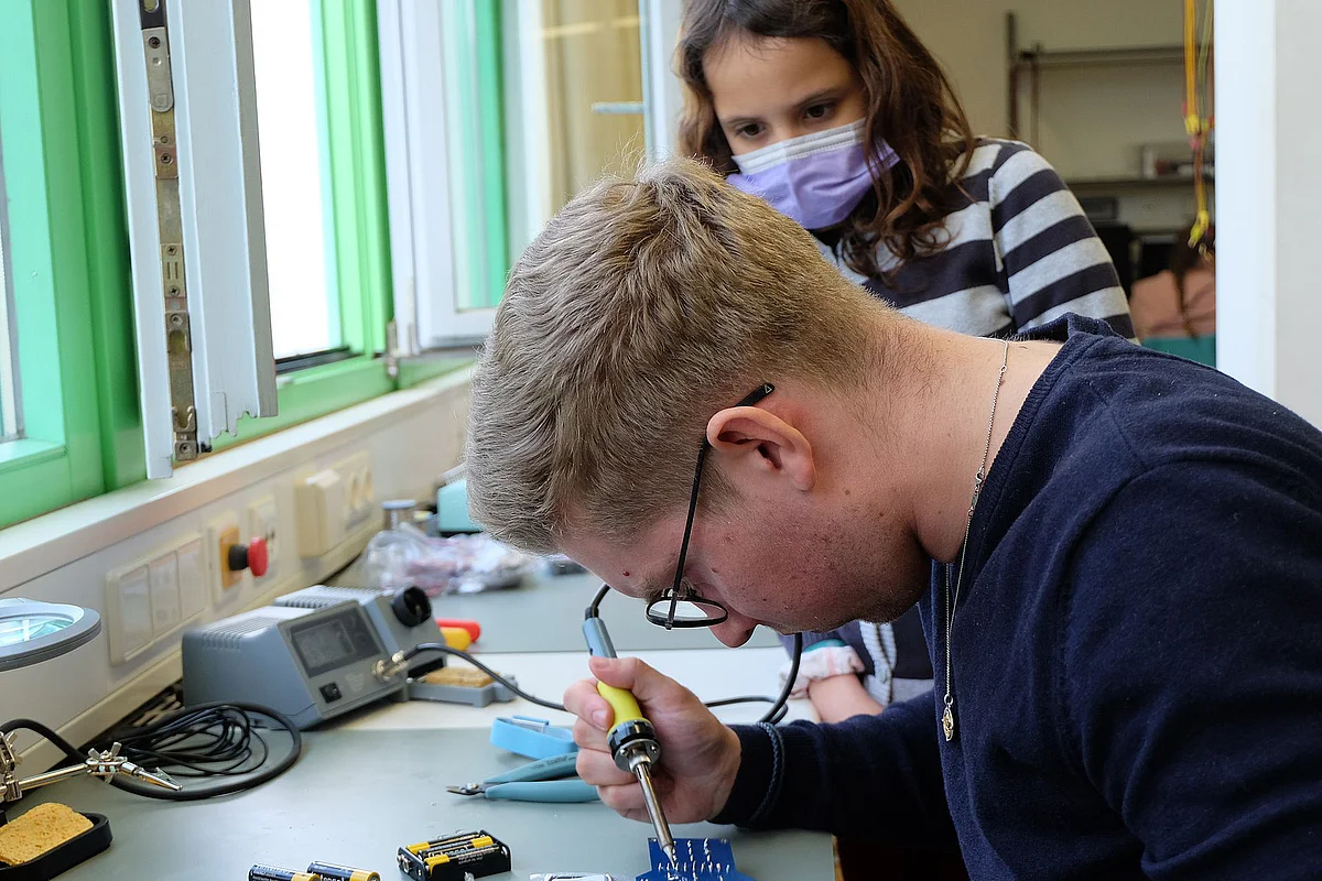 Studierender hilft Schülerin beim Löten