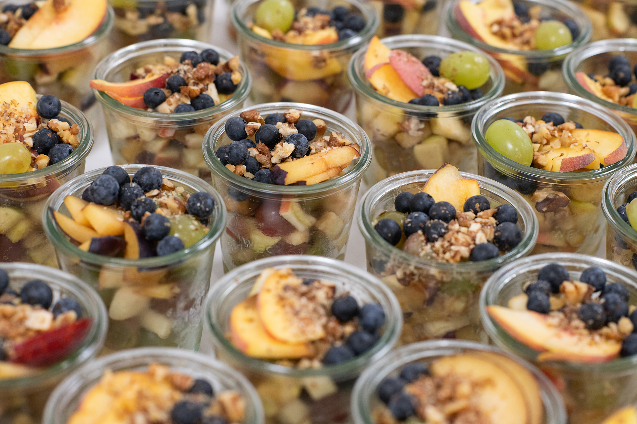 Dessert aus Fruchtstückchen und Nüssen, angerichtet in Gläsern auf einem Tisch 
