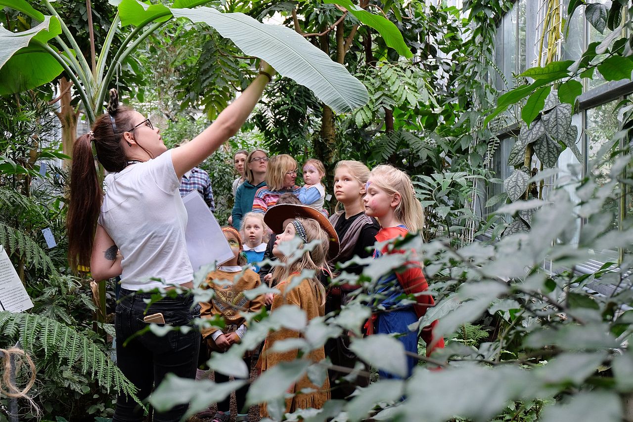 Im Gewächshaus zeigt eine Führerin des Botanischen Gartens einer Gruppe von Eltern mit verkleideten Kindern an Fasching spannende Pflanzen..