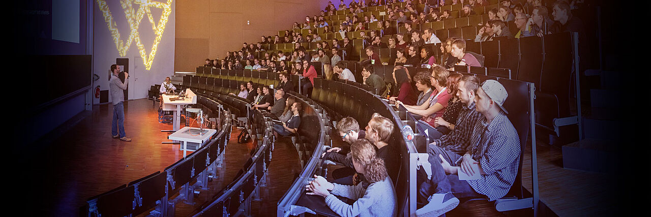 Ein Foto der Veranstaltung "Streiflicht 2019". Studierende in einem Hörsaal, die dem Moderator zuhören.