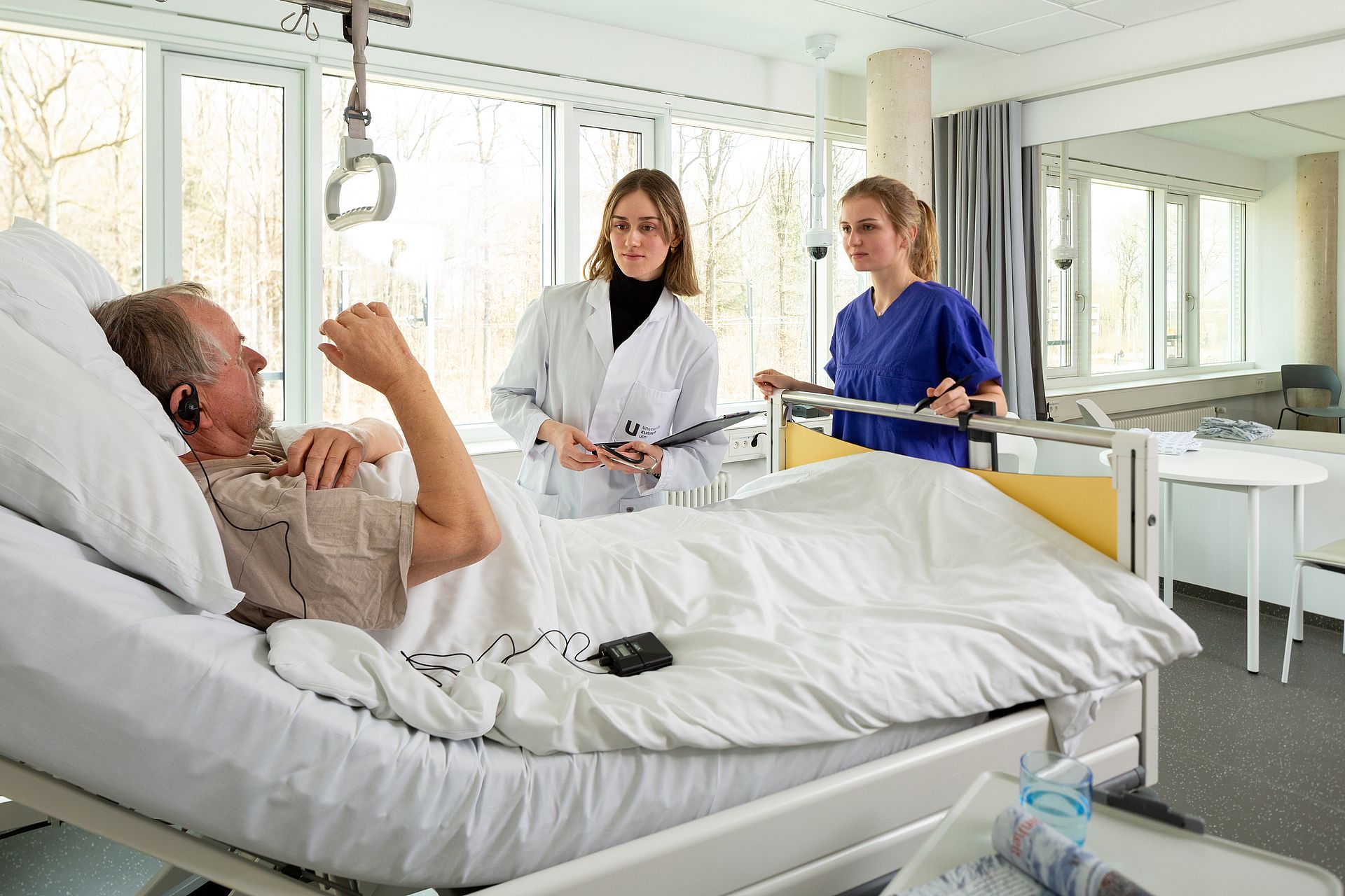 Zwei Studierende am Krankenbett eines männlichen Schauspielpatienten bei der "Visite" 