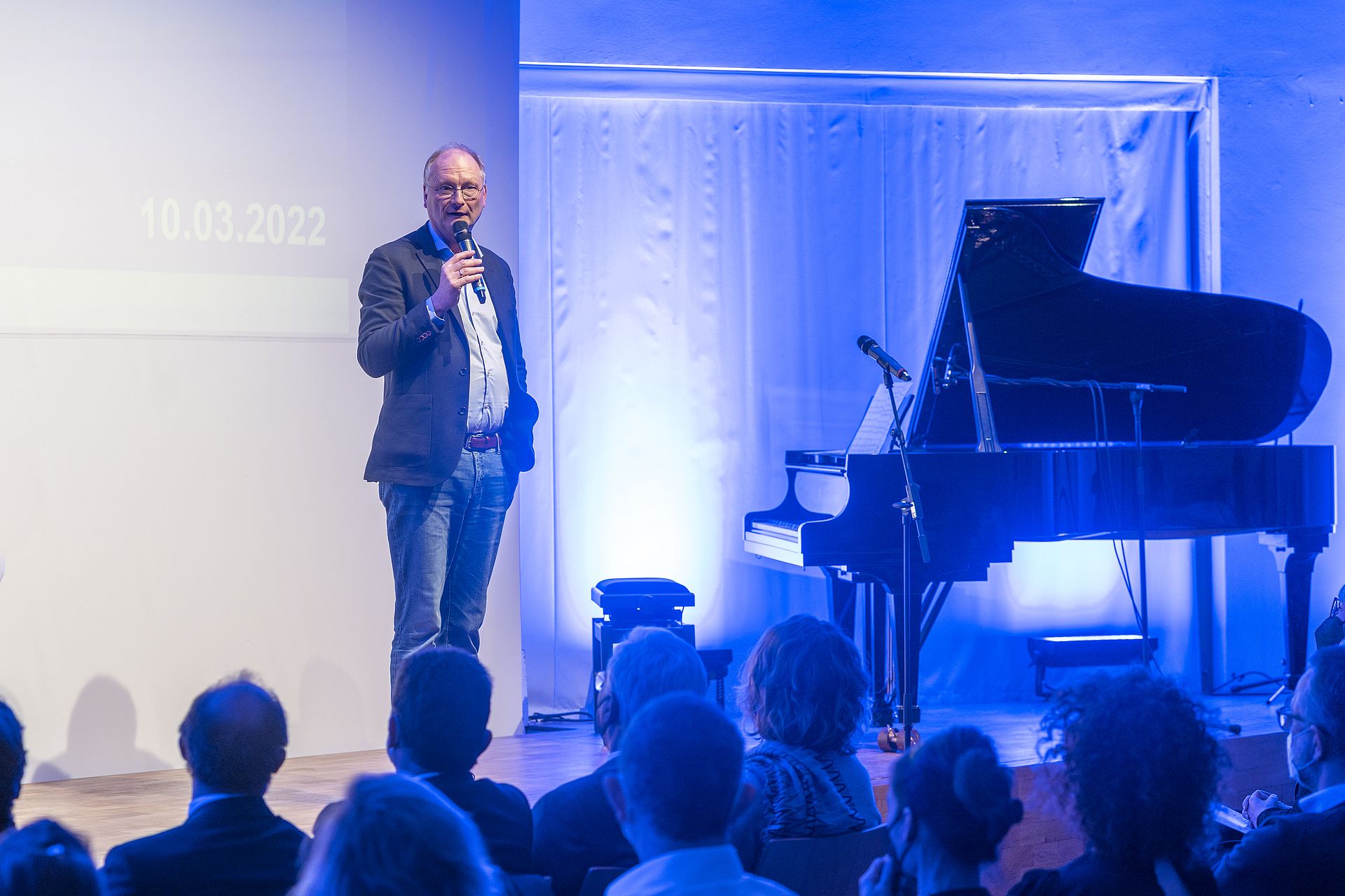 Mann mit Mikrofon vor Publikum bei Eröffnungsvortrag der Ulmer Denkanstöße