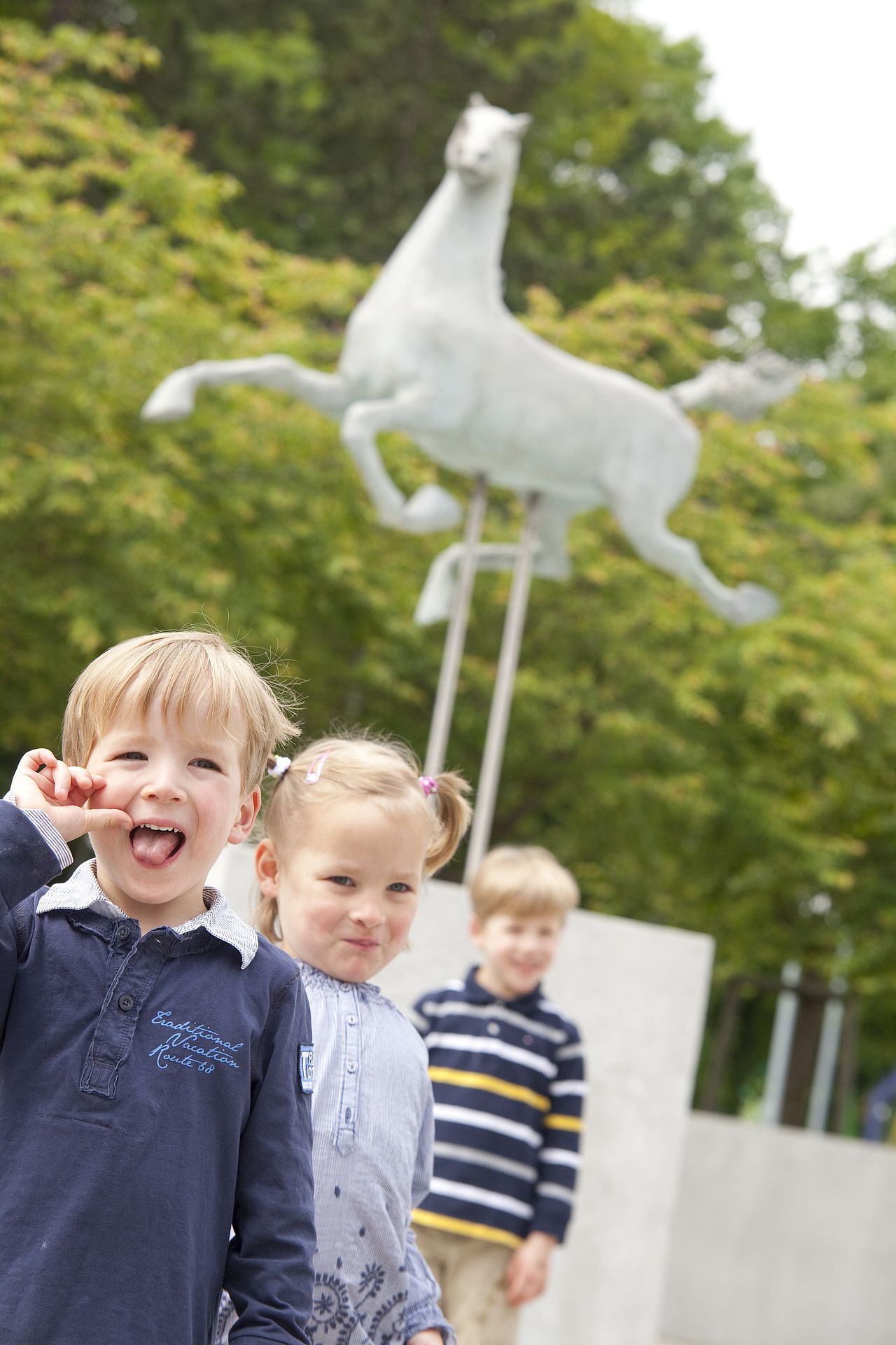 Drei Kinder stehen vor einer Statue vor dem Eingang der Ulmer Kinderklinik