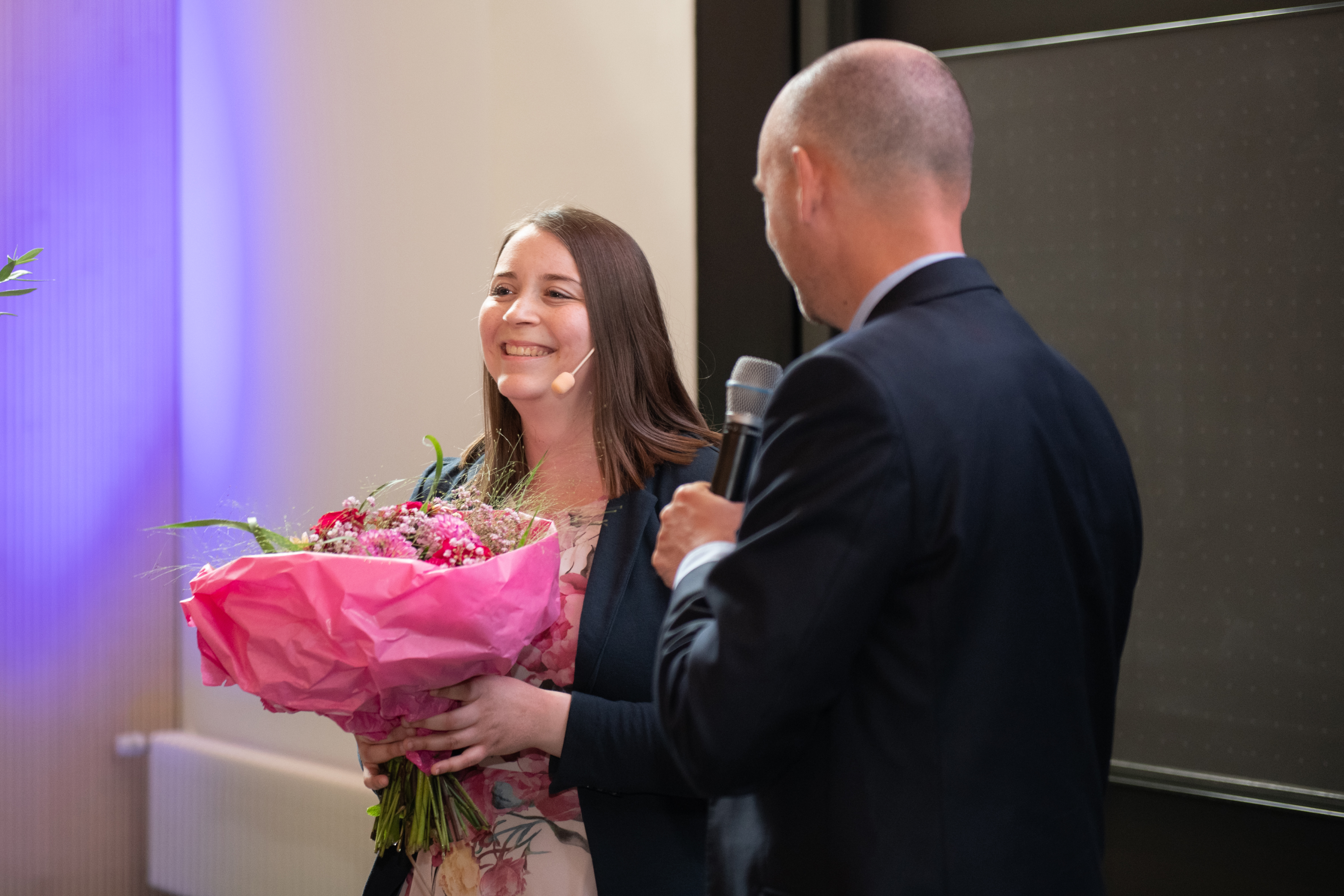 Frau mit Blumenstrauß in der Hand neben ihr ein Mann mit Mikrofon 