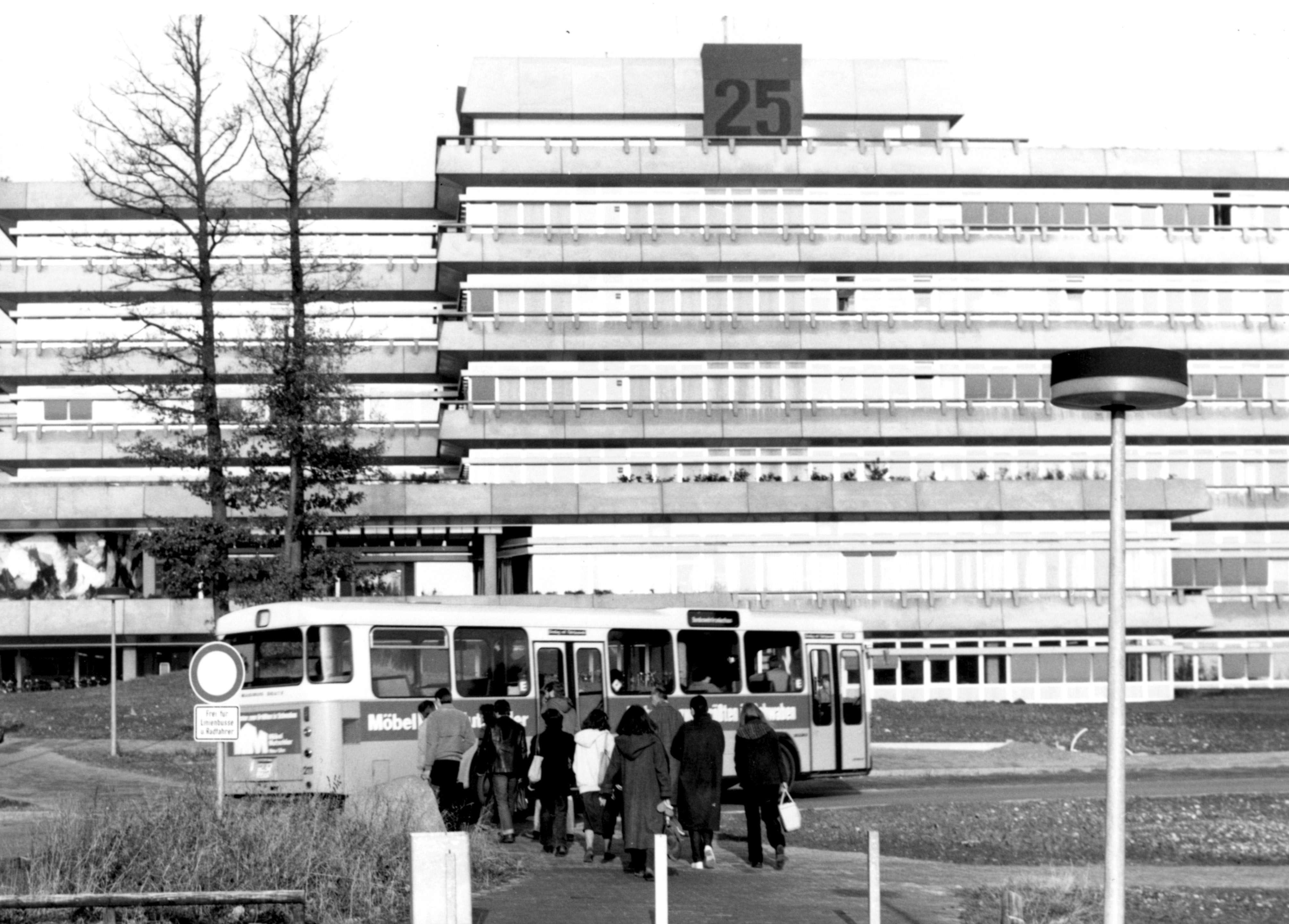 Südeingang in Schwarzweiß, Bus fährt durchs Bild, Menschengruppe läuft Richtung Uni