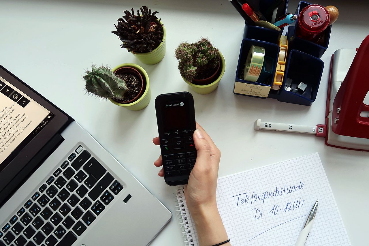 Eine Hand hält ein Telefon auf dem Schreibtisch 