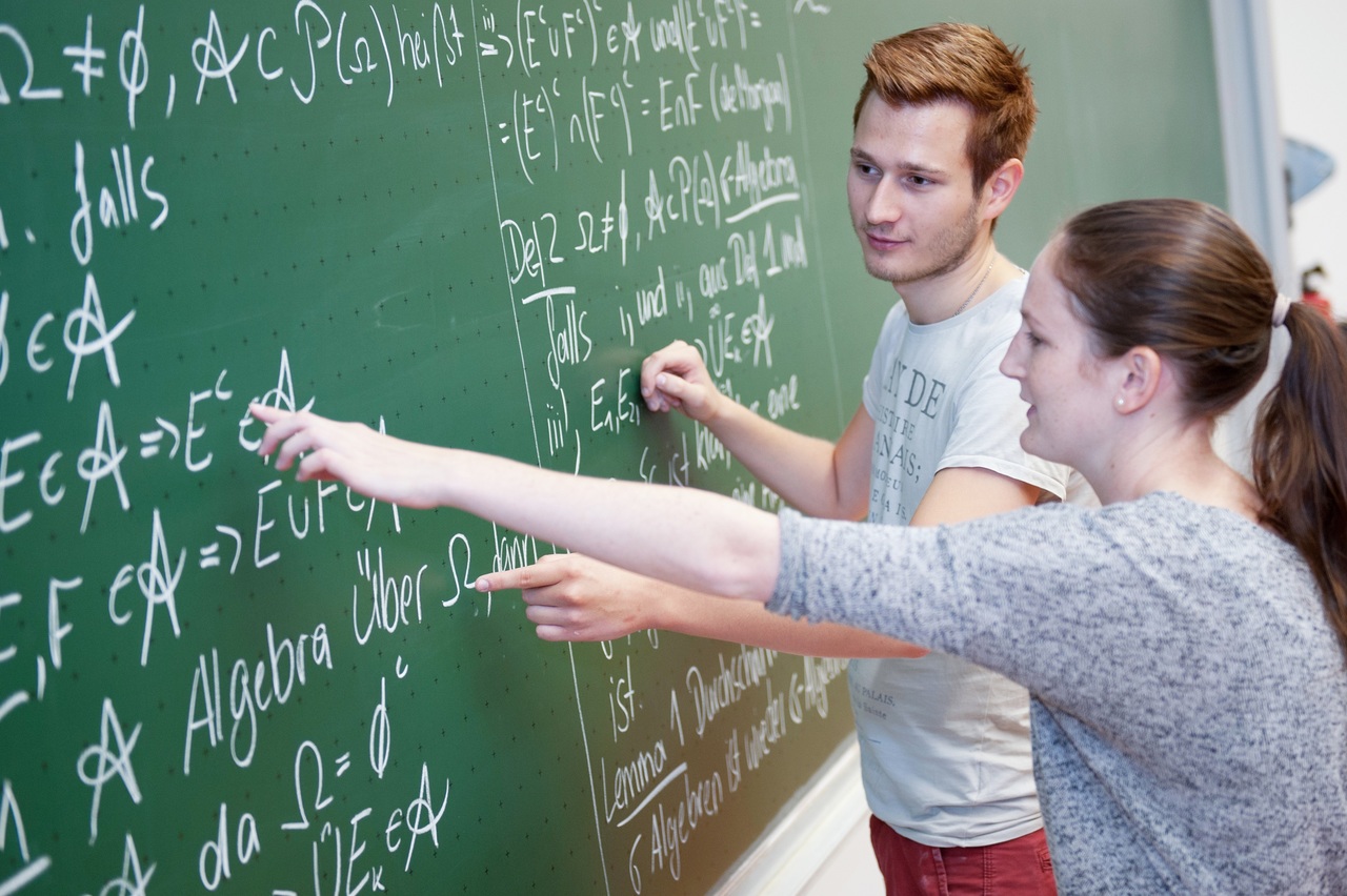 Mathematik Studierende mit Tutor erklärt eine Aufgabe an der Tafel