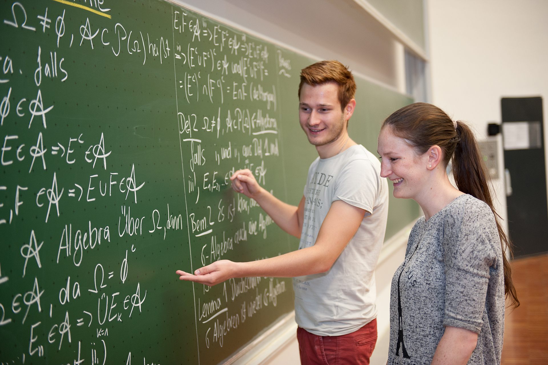 Zwei Studierende stehen an einer Tafel auf der Formeln zu sehen sind