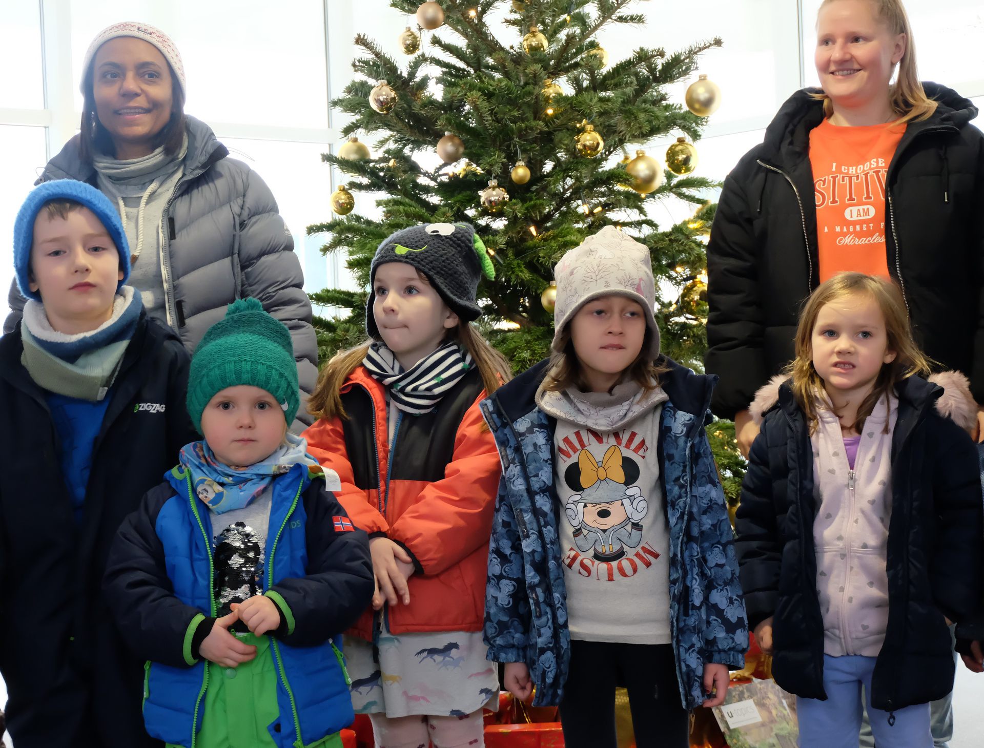 Kinder mit Erzieherinnen vor dem geschmückten Tannenbaum