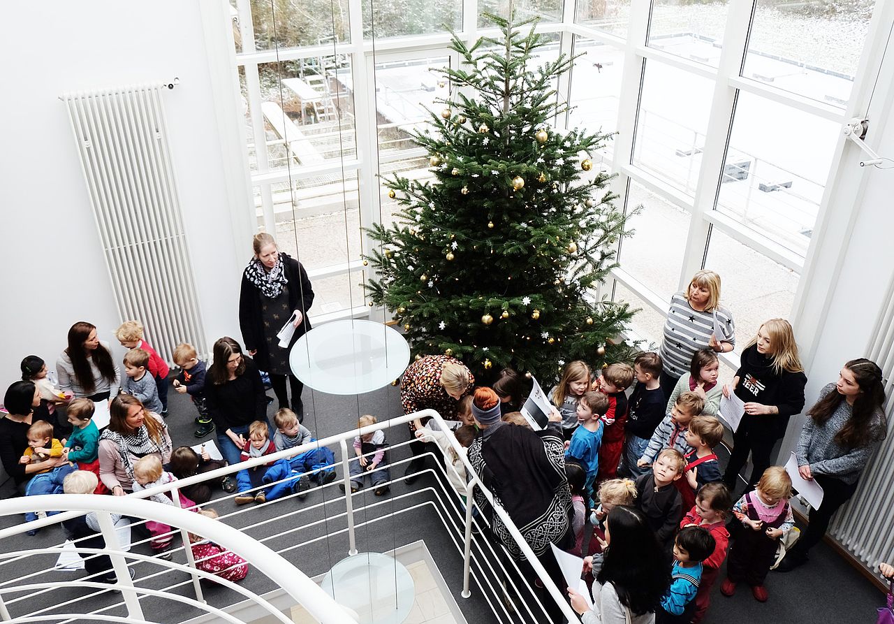 Krippen- und Kindergartenkinder und Erzieherinnen stehen vor dem Weihnachtsbaum