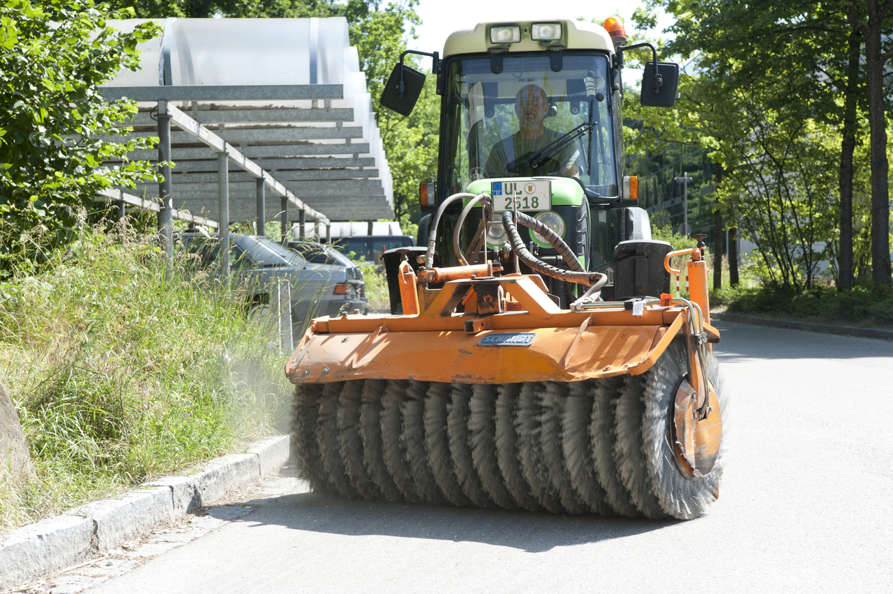 Hausmeister in der Kehrmaschine beim Reinigen des Gehweges